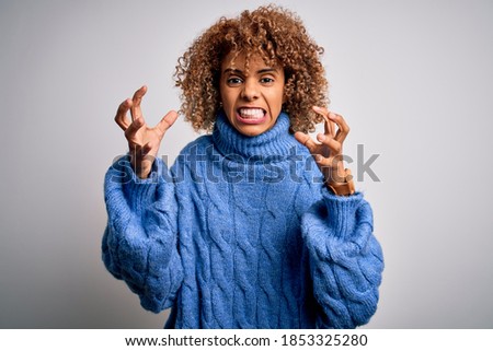 Young beautiful african american woman wearing turtleneck sweater over white background Shouting frustrated with rage, hands trying to strangle, yelling mad