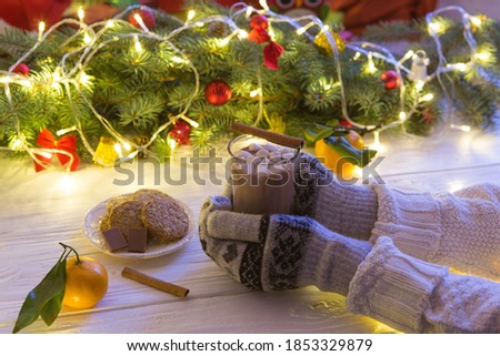 Woman hands ith cup of hot chocolate on christnas tree background.