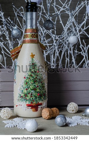A bottle with champagne, snowflakes, balls on the background of a box with white branches. Christmas decor.