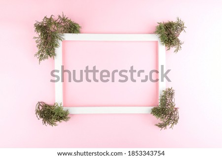 Festive elegant background. Blank photo frame on pastel pink background with fir tree twigs Christmas, New Year, birthday concept. Flat lay, top view, copy space