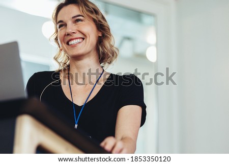 Confident businesswoman standing at podium. Smiling female business professional addressing a conference. Royalty-Free Stock Photo #1853350120