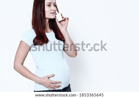 A woman is standing and burying her nose with a nasal spray. Girl stands on a white background and holding on to her stomach.  Royalty-Free Stock Photo #1853365645