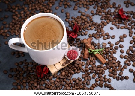 White cup full of coffee beans close up against the dark grey background. Coffee mug. Morning espresso.	