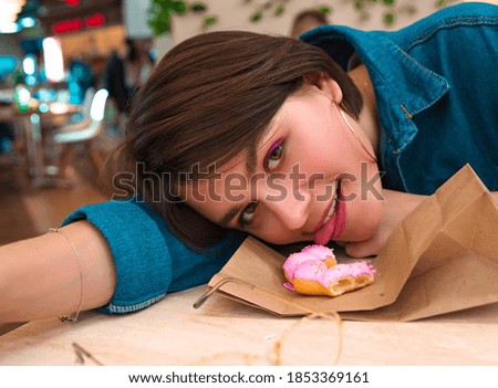 A girl eats a doughnut in a shopping center, leaning on a table