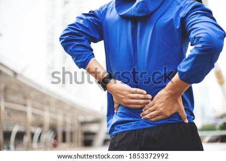 A man wearing a blue Windbreaker jacket., Back injury after exercise concept.It happens often in athletes practice overtain,Lifting heavy objects .In a Muscle inflammation concept. Royalty-Free Stock Photo #1853372992