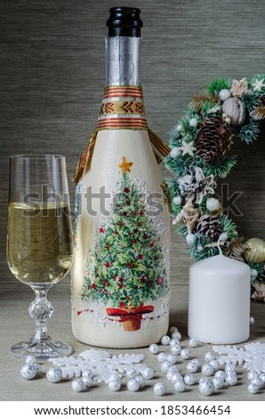 A bottle of champagne, a glass of champagne, a Christmas wreath, large snowflakes, a candle, artificial snow on a gray background.