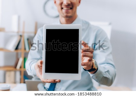 Cropped view of digital tablet with blank screen in hands of smiling businessman on blurred background
