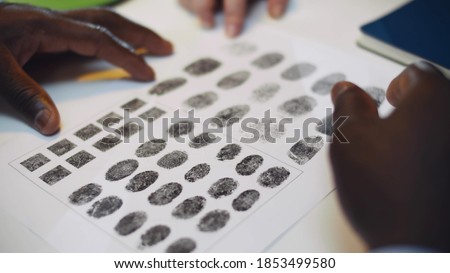 Close up of diverse police officers studying fingerprint card working at police station. African and caucasian policemen hands pointing at fingerprints sample on paper investigating crime in office Royalty-Free Stock Photo #1853499580