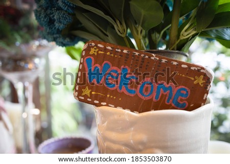 Brown wooden signboard with "Welcome" text put in the flower pot inside the restaurant cafe to greeting guests after back to business from covid-19 lockdown.