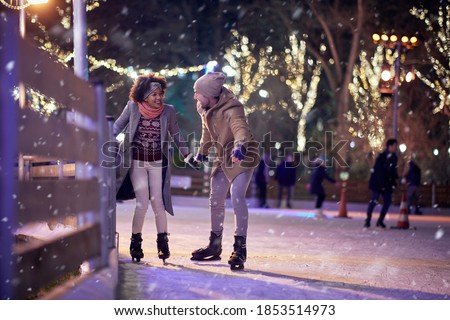 A young couple enjoying learning to skate at ice rink on a beautiful magical night. Skating, closeness, love, together