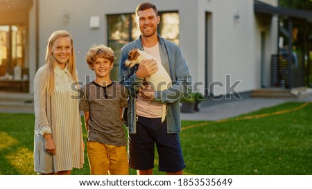 Portrait of Smiling Father, Mother and Son Posing with Smooth Fox Terrier Retriever Dog that Dad Holds. Idyllic Happy Family Have Fun with Loyal Pedigree Dog Outdoors in Summer House Backyard