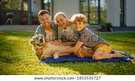 Portrait of Father, Mother, and Son Having Picnic on the Lawn, Posing with Happy Golden Retriever Dog. Idyllic Family Have Fun with Loyal Pedigree Doggy Outdoors in Summer House Backyard.