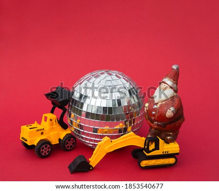 concept for Christmas business greetings, New Year winter holidays in a construction company. toy loader and excavator models, Santa souvenir figurine, mirror disco ball on red background