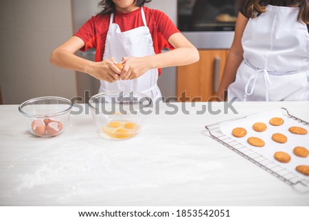 Small and short children cooking dough together in the kitchen with eggs and biscuits.