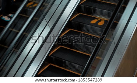 Black staircase escolator in a shopping center with a footprint sign for keeping a social distance