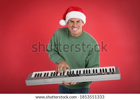 Man in Santa hat playing synthesizer on red background. Christmas music
