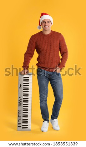 Man in Santa hat with synthesizer on yellow background. Christmas music