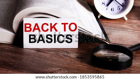 BACK TO BASICS written on a white card near an open book, alarm clock and magnifying glass