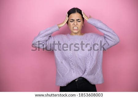 Beautiful woman wearing a casual violet sweater over pink background suffering from headache desperate and stressed because pain and migraine with her hands on head