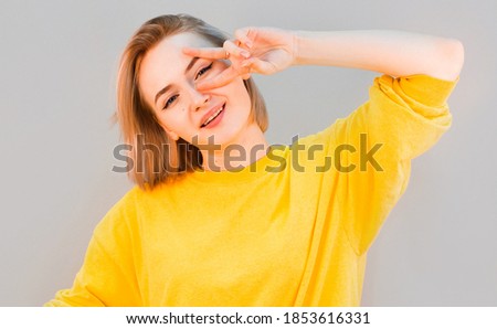 Portrait of cute sweet gorgeous nice lady with her blond hairstyle she give v-sign near eye make hollywood white smile stand isolated on gray background