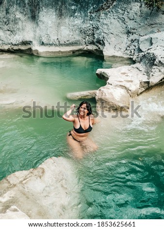 A vertical shot of a young female swimming in a pond near a cliff
