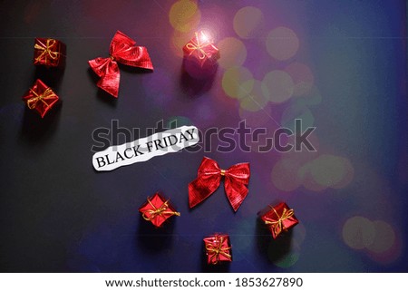 Black Friday sale business concept. Advertising message on a paper sheet and red gifts on a black background. Festive dark background with blurred bokeh. Social media, mixed media.