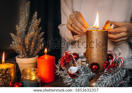 Close up of lighting first candle on Advent Wreath Celebrating Christmas or new year holidays. warm lights, xmas tree winter home interior decorations. hand holding match to fire candle. Wallpaper