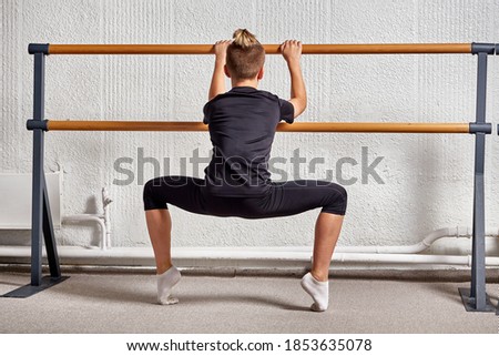 Back view of a young man in sportswear dancing ballet in a classroom. Training in ballet and gymnastics.