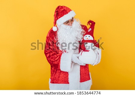 Santa Claus holding a snowman on yellow background. Christmas concept