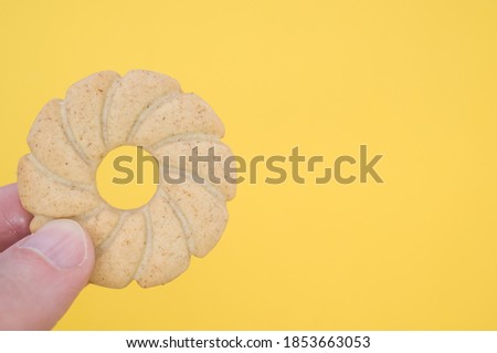A hand holding a sun shaped cookie on yellow background with a copy space