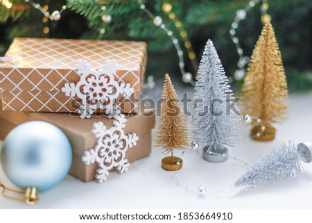 Christmas presents and gift boxes wrapped in kraft paper on a wooden table with gold and silver decorative Christmas trees, fir-tree branches, and decoration. New Year, Christmas concept. 