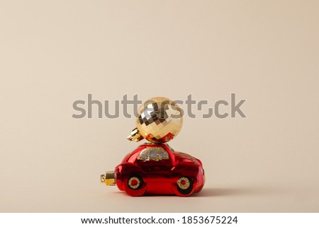 Red toy car delivering a Christmas gold ball on the roof on a beige background. Merry Christmas and Happy New Year concept.