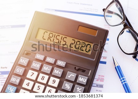 The word "crisis 2020" is written on the canculator display, on the desktop with financial documents, glasses and a pen. Business concept.