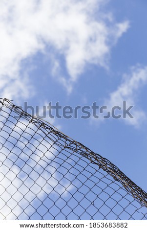we see the blue sky with white clouds through a wire fence