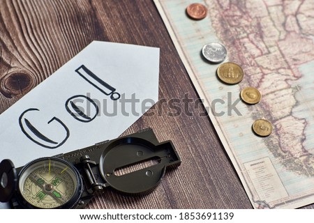 A top view closeup of a compass placed on a wooden table next to an ancient map with coins