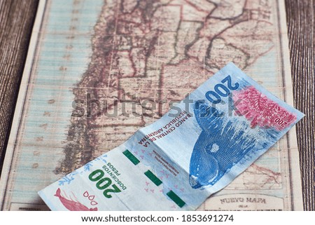 A top view closeup of 200 Argentinian pesos placed on an ancient map on a wooden table