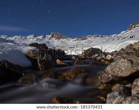 Flowing water in a wintry alpine landscape at full moon