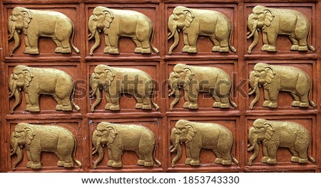 Picture of the wall decorated with the relief of elephants. The golden elephant is in a rectangular brown frame. Elephants are auspicious animals and are therefore popular to decorate important places