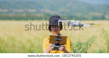 Mini drone flying with asia girl control at outdoor middle of field for your safety first, concept easy to fly drone