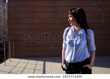 modern photographer happy girl in a leather cut for the camera against the backdrop of skyscrapers. woman wearing a blue shirt, black shorts and white trendy sneakers space for text smm lady
