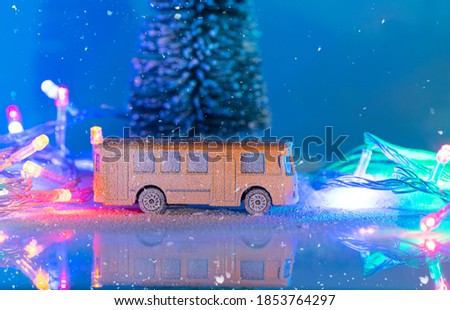 Miniature yellow bus and fir tree during snowfall, imitation of night time with garland. Christmas decoration, Christmas postcard with space for text