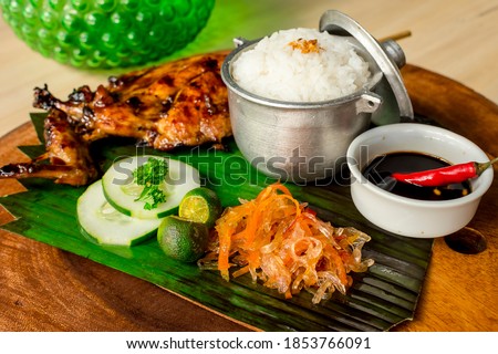 Chicken Inasal served with Garlic Rice, cucumber and Atchara. On a banana leaf on top of wooden platter. It is popular grilled dish from the Western Visayas region of the Philippines Royalty-Free Stock Photo #1853766091