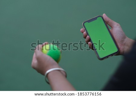 over shoulder view of people holding green screen smart phone while holding tennis ball 