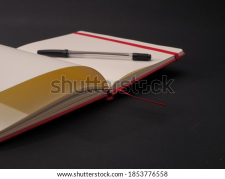 A closeup shot of an open and empty notebook for text with a pen isolated on dark background