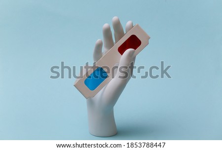 White mannequin hand holds paper 3d glasses on blue background
