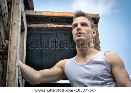Young man against old rusty metal door and wood, photographed from below.