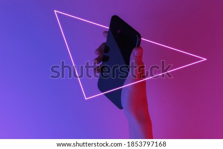 Female hand holds a smartphone. Creative pop art pink blue neon color. Trendy gradient illumination. Night light