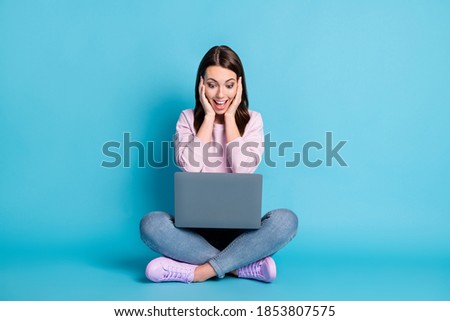 Full length photo shocked girl sit floor legs crossed study remote laptop pass university exam get wow email touch hands face wear lilac pullover jeans isolated blue color background