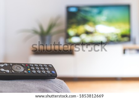 TV remote control in the foreground, tv in the blurry background. Streaming.