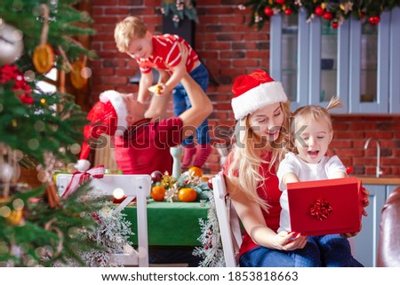 Happy family is sitting at festive table in kitchen. Woman, man with kids are celebrating new year holidays, opening presents. Christmas breakfast. Parents are spending  time with children at home.